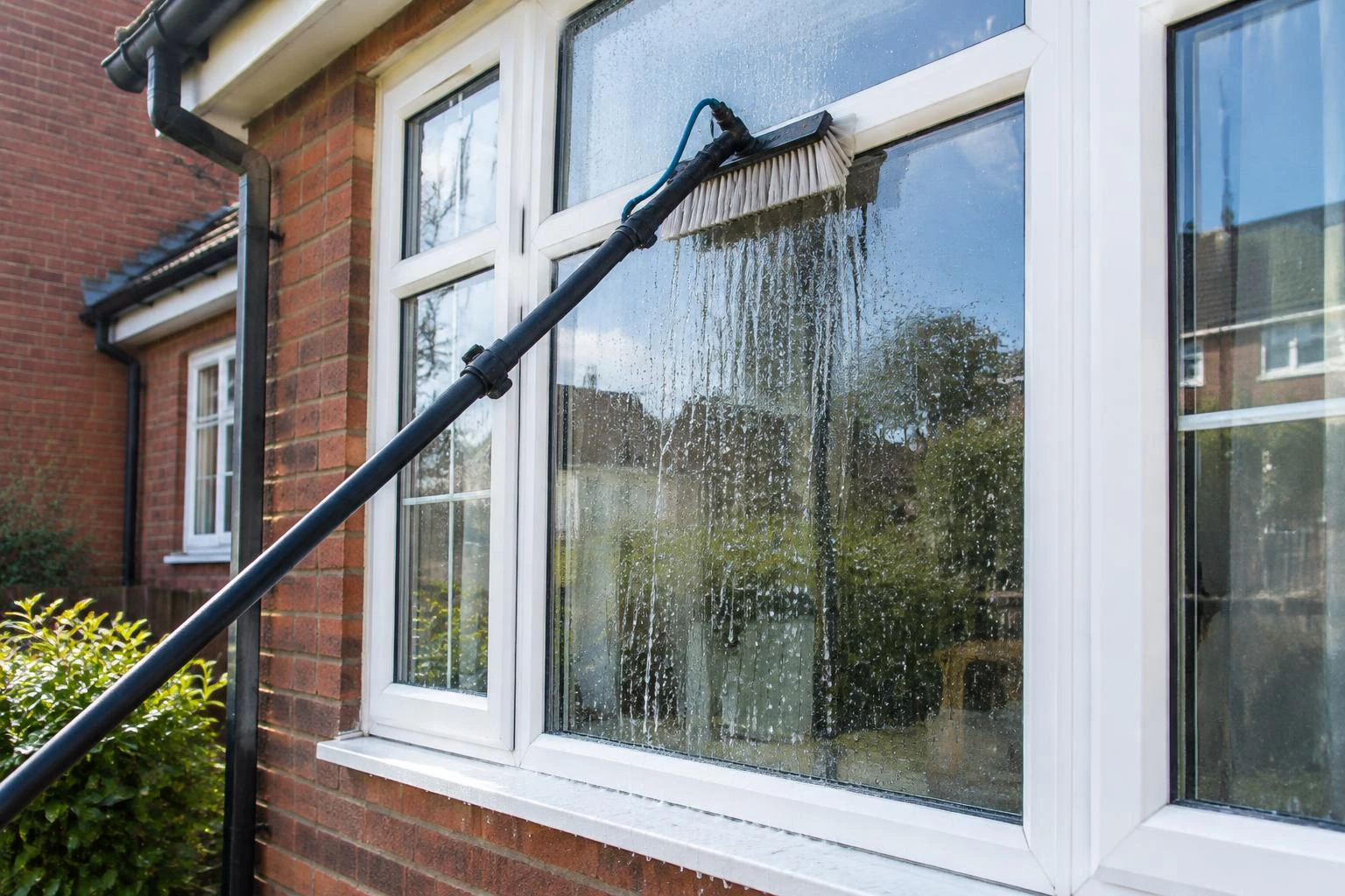 Water-fed brush washing glass in white-framed domestic windows